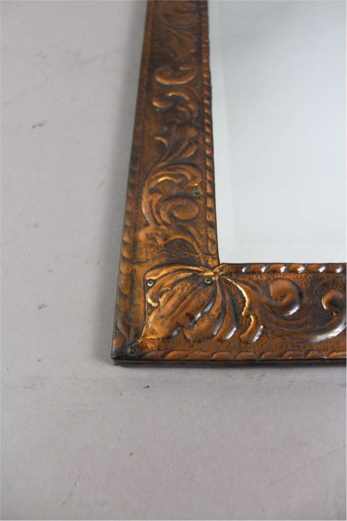 Copper arts and crafts mirror with scrolling leaf design.